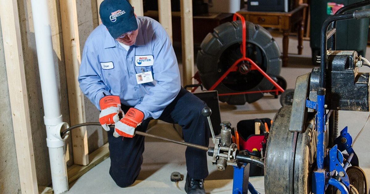 Plumber feeding a drain-cleaning cable from a powered machine into a waste pipe