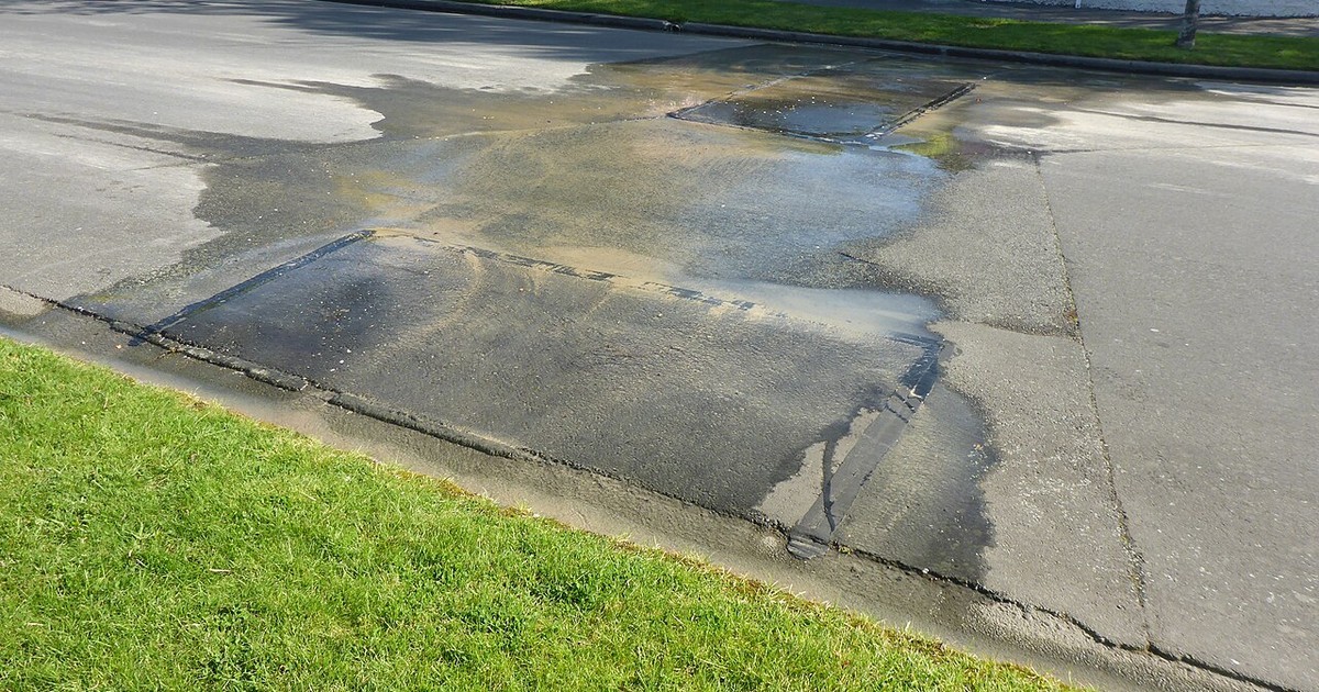 Water pooling across a paved path and lawn where a leak has surfaced