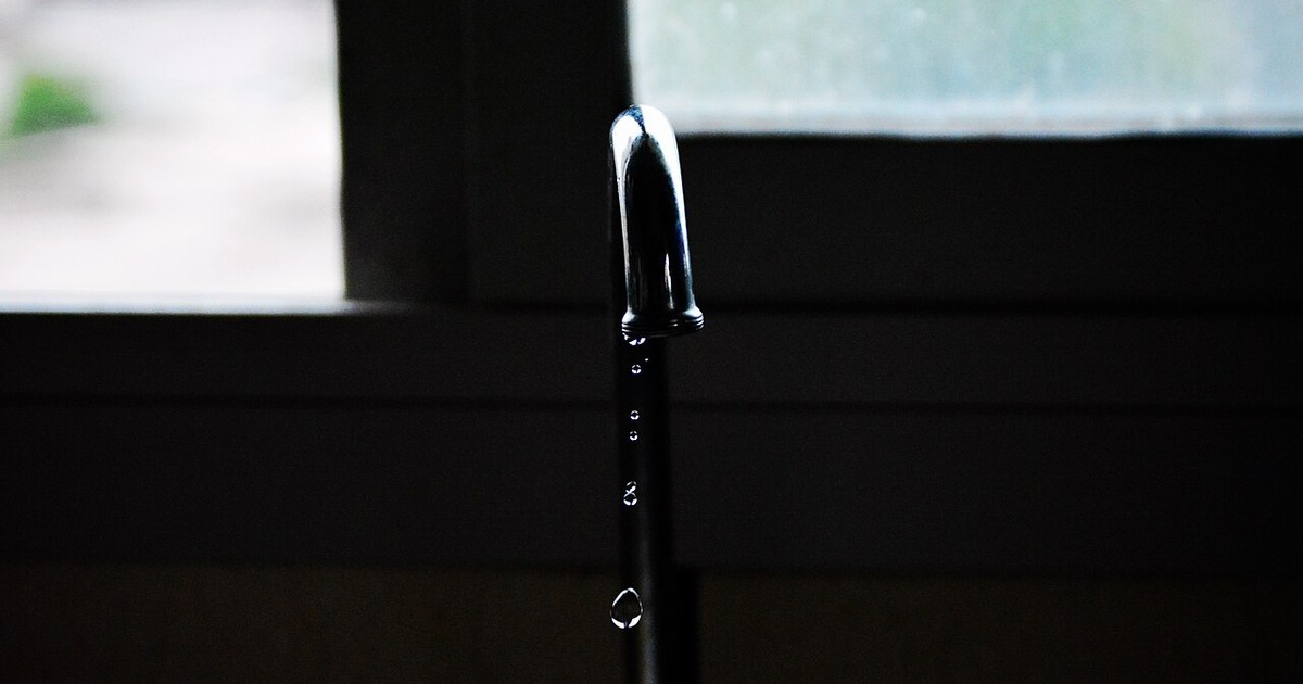 A chrome tap with a drop of water hanging from the spout