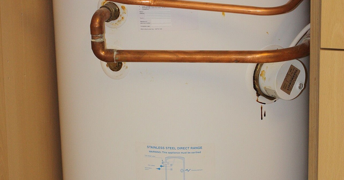 A white hot water storage cylinder with copper pipework in a laundry