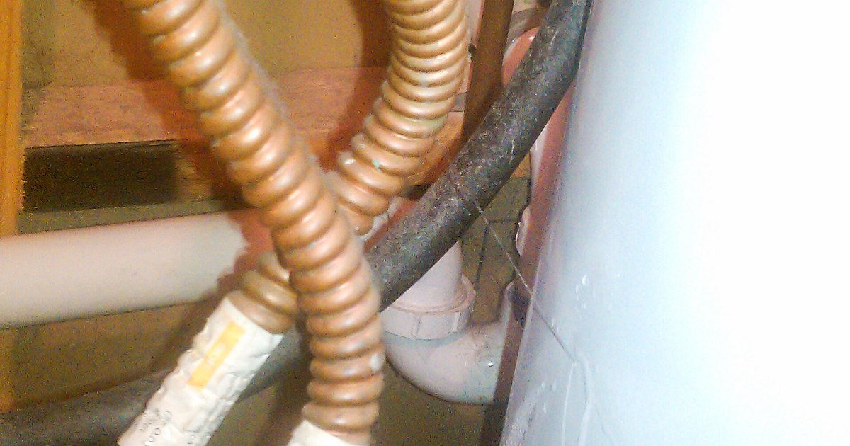 Flexible hoses and a copper pipe connection at a water heater, with water on the floor below