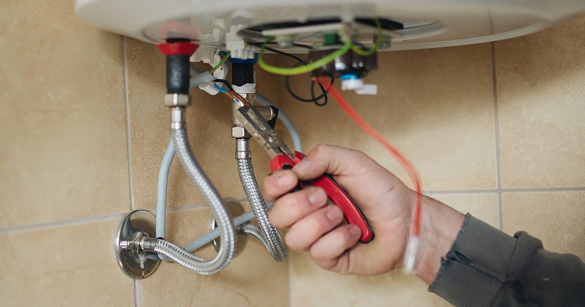 Plumber working on wiring and fittings around a water heater