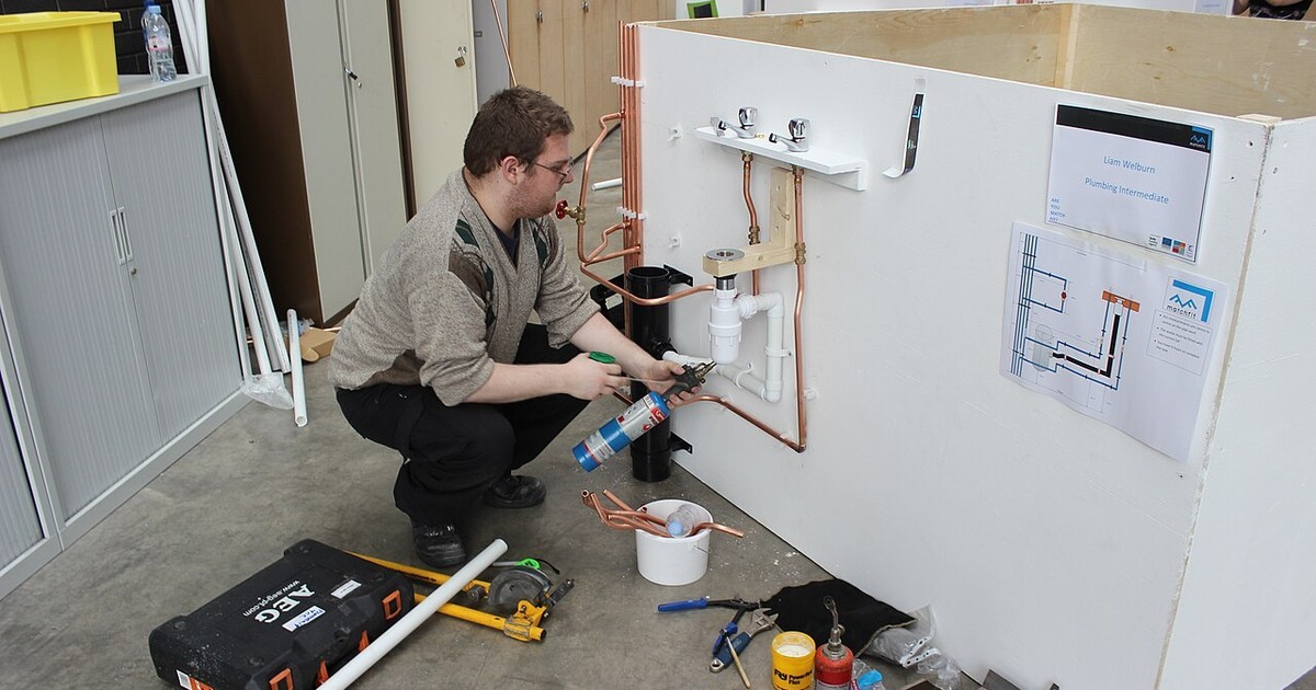 A plumber installing pipework and fittings against a wall