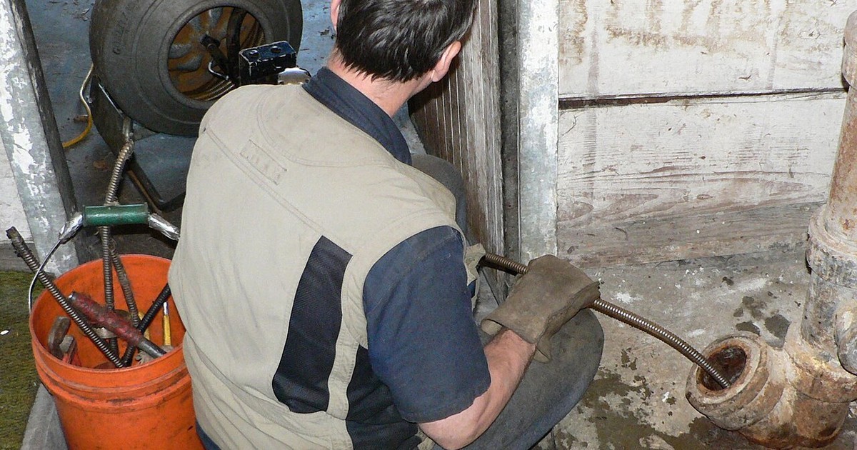 A plumber clearing a drain pipe with hand tools