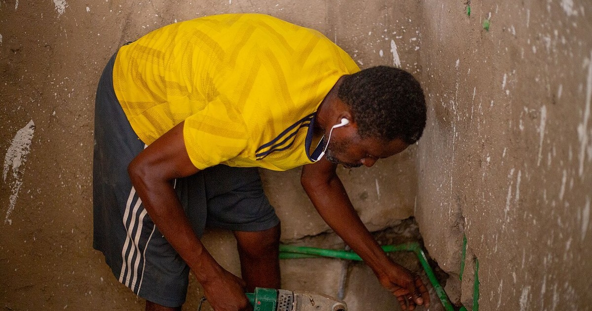 Plumber kneeling to work on pipework where it meets the floor and wall