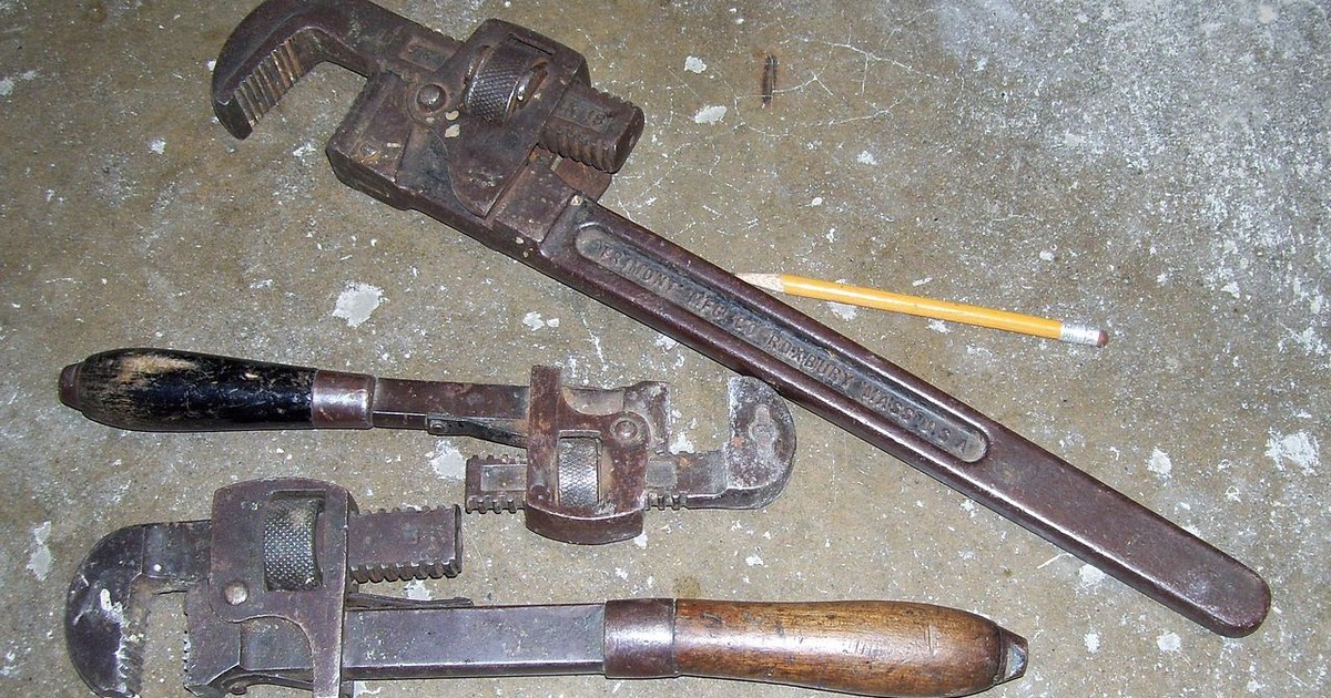 Two pipe wrenches on a concrete floor, the tools used to open and repair pipework