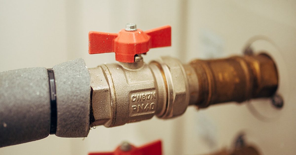 Close-up of a red-handled plumbing valve on copper pipe